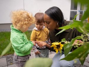 Eine Erzieherin betrachtet zusammen mit Kindern eine Sonnenblume genau.